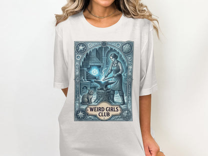 T-shirt graphic with a woman blacksmithing next to a cat, "Weird Girls Club" text.