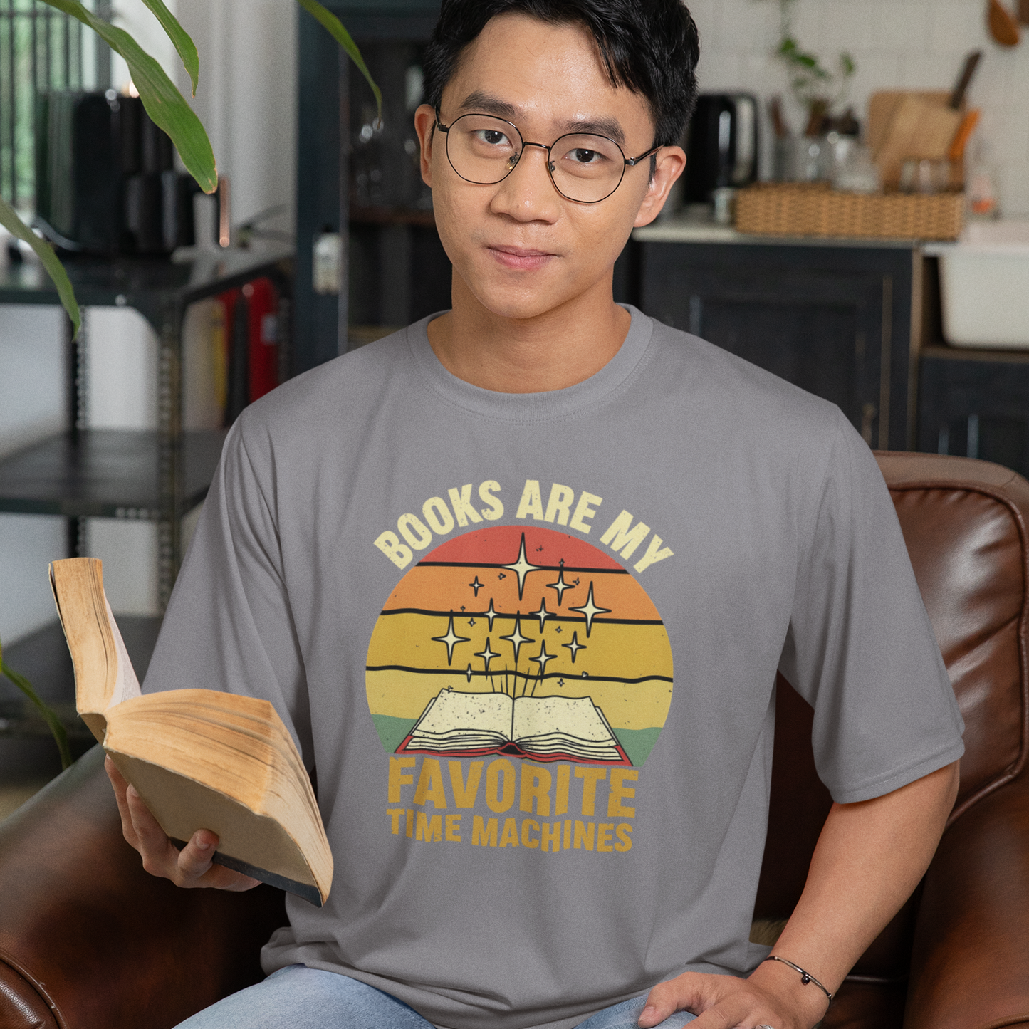 Person sitting on a couch holding a book, wearing a t-shirt with a graphic design, in a home setting.