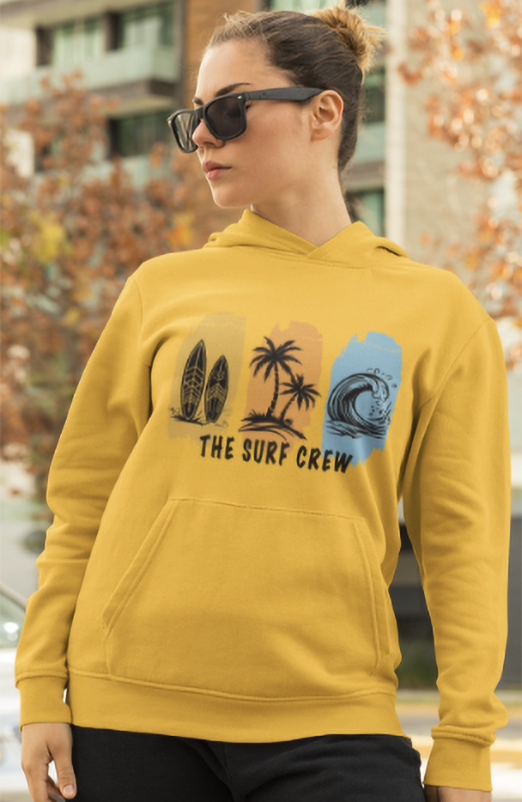 Person wearing a mustard yellow hoodie with 'The Surf Crew' design outdoors.