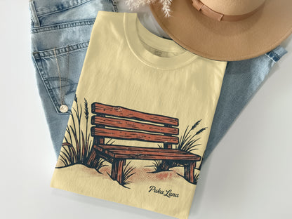 Cream t-shirt with a wood bench and grass illustration and "Puka Luna" text.