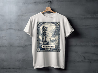 White t-shirt featuring a framed illustration of a woman with binoculars and a dinosaur.