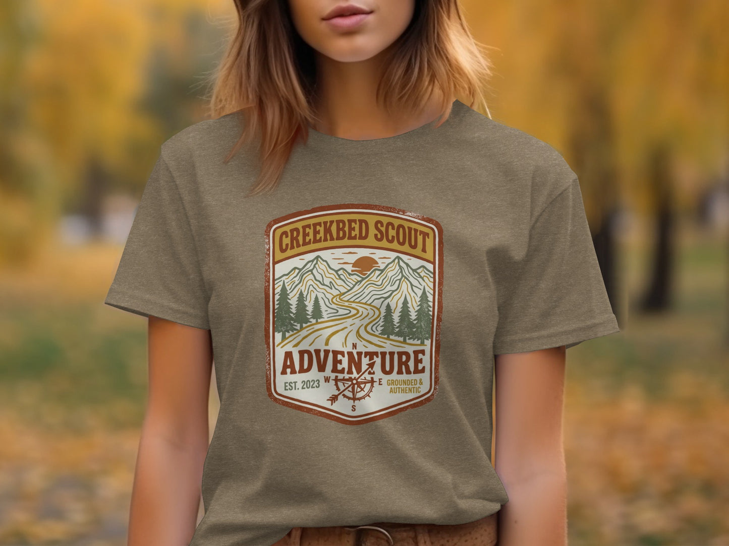Rugged Creekbed Scout Adventure Emblem Wilderness Shirt: Creek Scout Adventure logo with mountains, road, and compass on a brown t-shirt.
