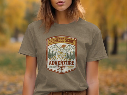 Rugged Creekbed Scout Adventure Emblem Wilderness Shirt: Creek Scout Adventure logo with mountains, road, and compass on a brown t-shirt.