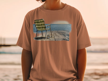 T-shirt featuring a printed graphic of a beach chair and cooler by the ocean.