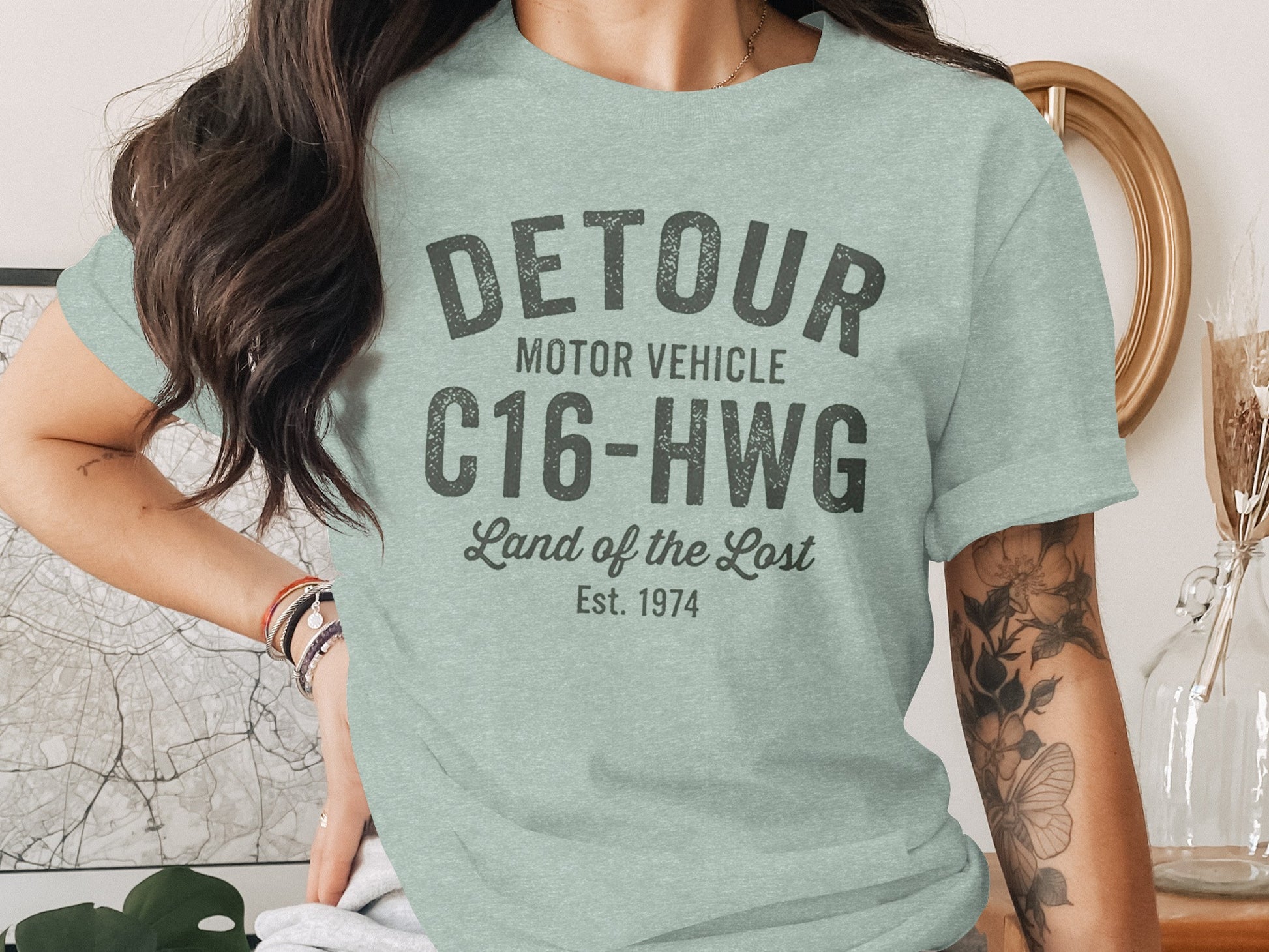 Light green t-shirt with "DETOUR MOTOR VEHICLE C16-HWG Land of the Lost Est. 1974" text.