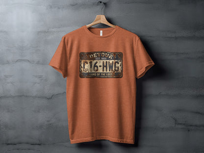 Land of the Lost Detour Plate: The Explorer's Adventure Tee: Orange t-shirt with a license plate graphic reading "DETOUR EST. 1955 C16-HWG LAND OF THE LOST".
