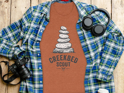 Creekbed Scout Cairn Graphic: The Explorer's Adventure Tee: Plaid shirt with balanced rock art and "Creekbed Scout" text.