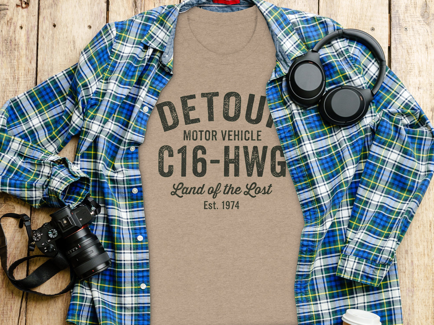 Tan t-shirt with "DETOUR MOTOR VEHICLE Land of the Lost Est. 1974" printed on it.