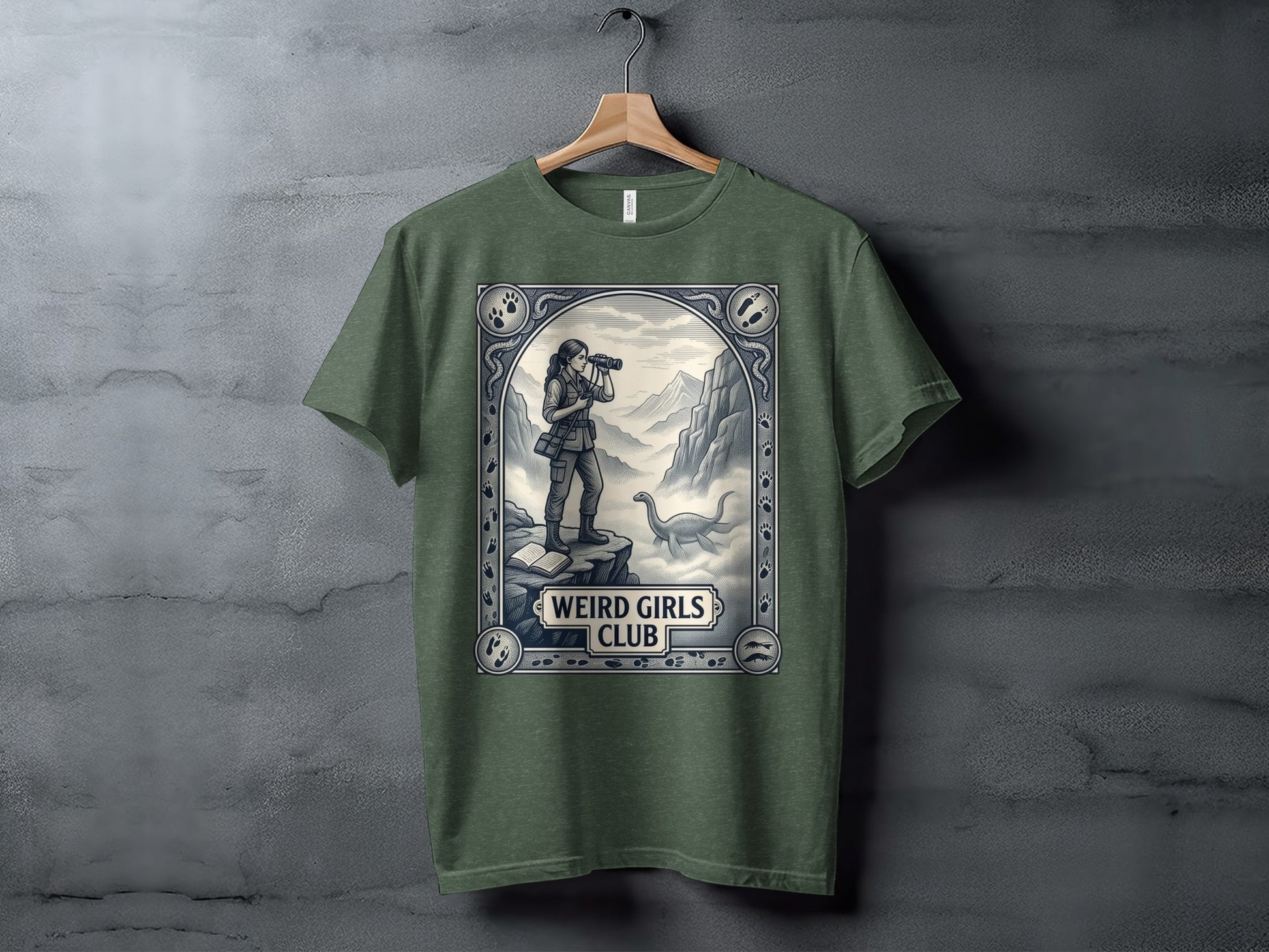 Olive green t-shirt featuring a "Weird Girls Club" design with a woman observing a dinosaur.
