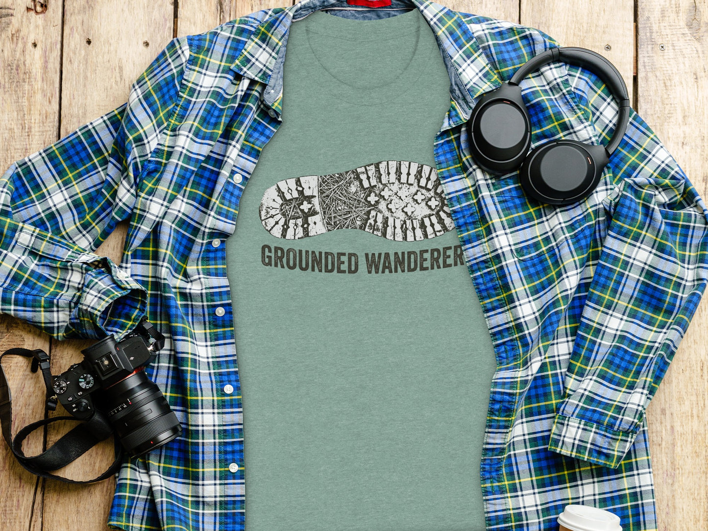 Grounded Wanderer Boot Print | Vintage Outdoor Apparel: Green t-shirt with "GROUNDED WANDERER" and boot print, next to camera and headphones.