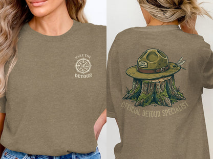 Brown t-shirt with "Take the Detour" compass logo on front and park ranger hat on stump on back.