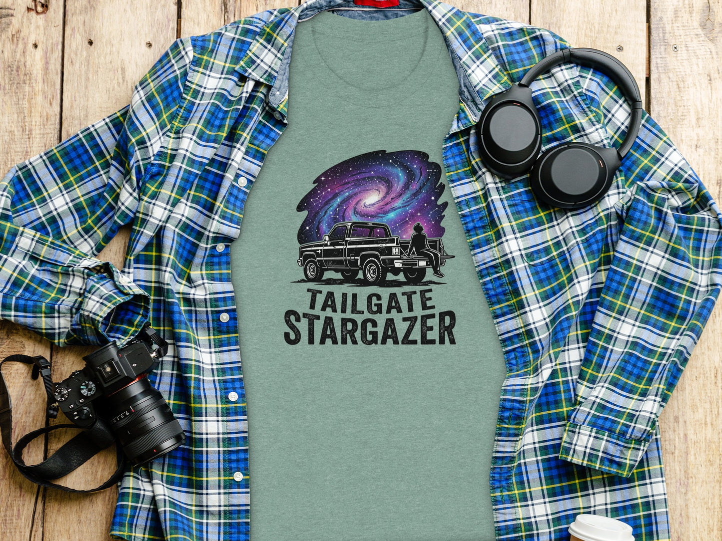 Heritage Cosmic Tailgate Stargazer Nomad Tee: Green t-shirt with a galaxy and truck graphic, paired with a plaid shirt and headphones.