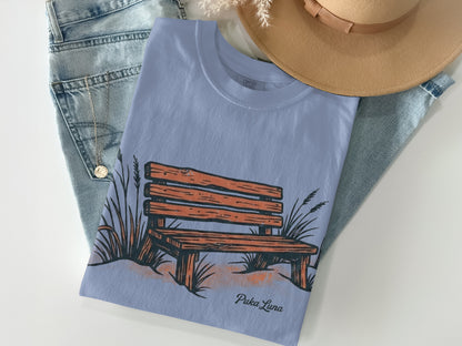 Light blue t-shirt with a graphic of a wooden bench and reeds, and the text "Puka Luna".