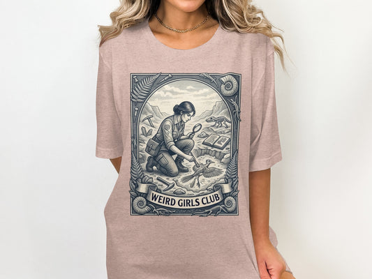 T-shirt graphic of a woman examining a fossil with "Weird Girls Club" text.