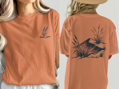 Orange t-shirt with "Puka Luna" text and grass and bird illustration.