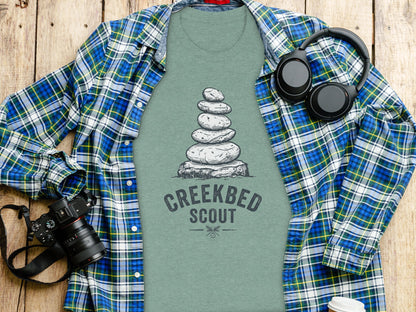Creekbed Scout Cairn Graphic: The Explorer's Adventure Tee: Green t-shirt with stacked stones and "Creekbed Scout" text.