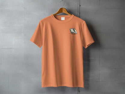 Orange t-shirt with conch shell logo on a gray concrete background.