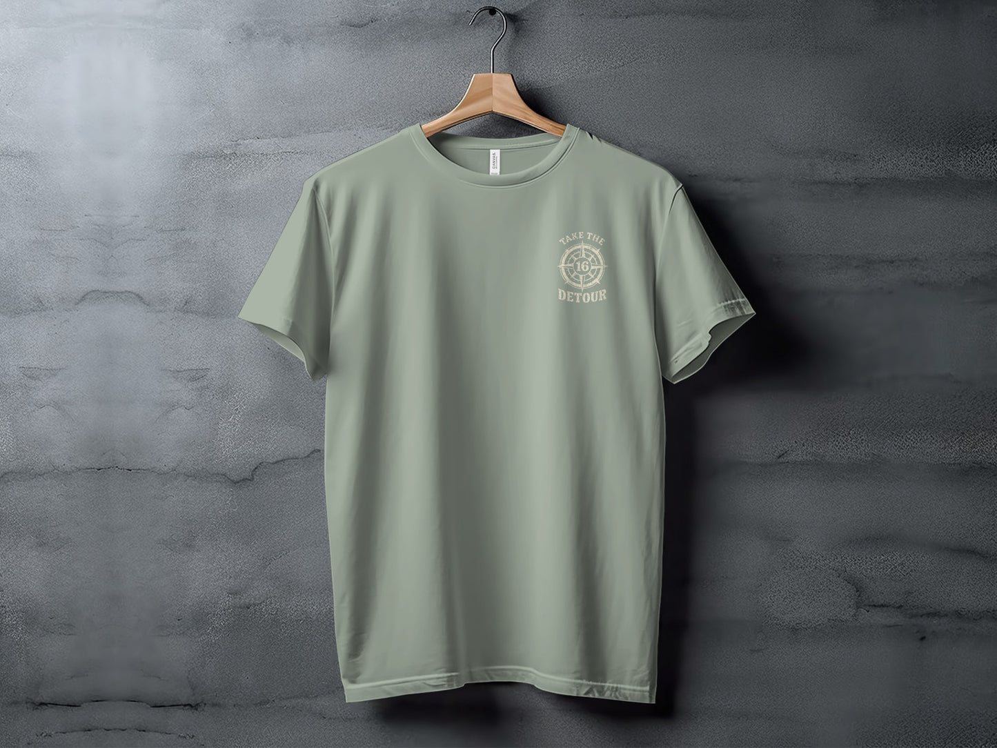 Sage green t-shirt with "Take the Detour" compass design, displayed on a hanger.