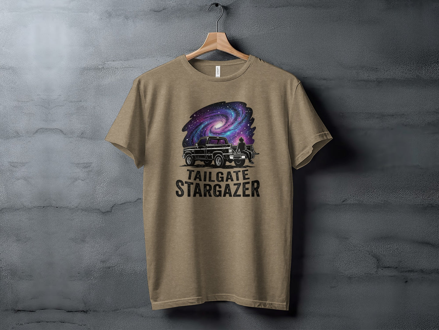Heritage Cosmic Tailgate Stargazer Nomad Tee: Truck and galaxy design with "Tailgate Stargazer" text on a tan t-shirt.