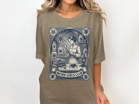 T-shirt graphic: woman examining spider under magnifying glass, "Weird Girls Club" text banner.