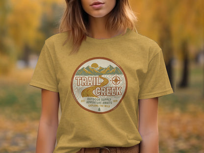 Heritage Heritage Explorer Trail Creek Nomad Tee: Gold t-shirt with "Trail Creek Outdoor Supply Adventure Awaits" circular graphic.