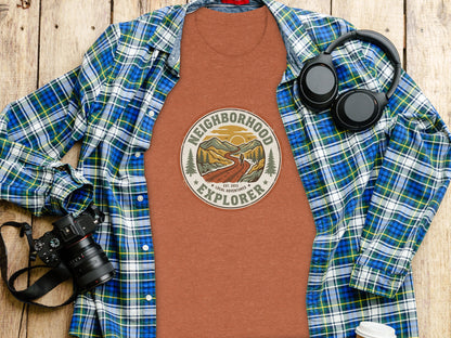 The Original Neighborhood Explorer Adventure Adventure Top: T-shirt with "Neighborhood Explorer" graphic, headphones, and camera on wooden surface.