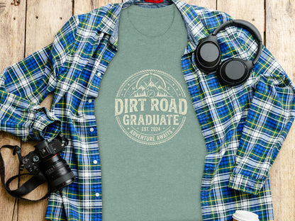 Dirt Road Graduate '24 Adventure | Vintage Outdoor Apparel: Green t-shirt with "Dirt Road Graduate" design, open plaid shirt, headphones, and camera.