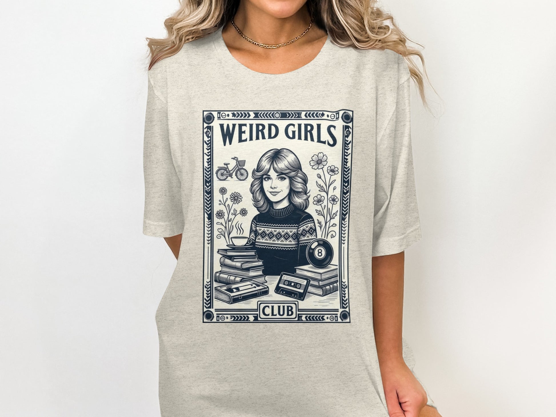 Cream t-shirt with "WEIRD GIRLS CLUB" text and retro illustration of a girl with books and cassette tape.