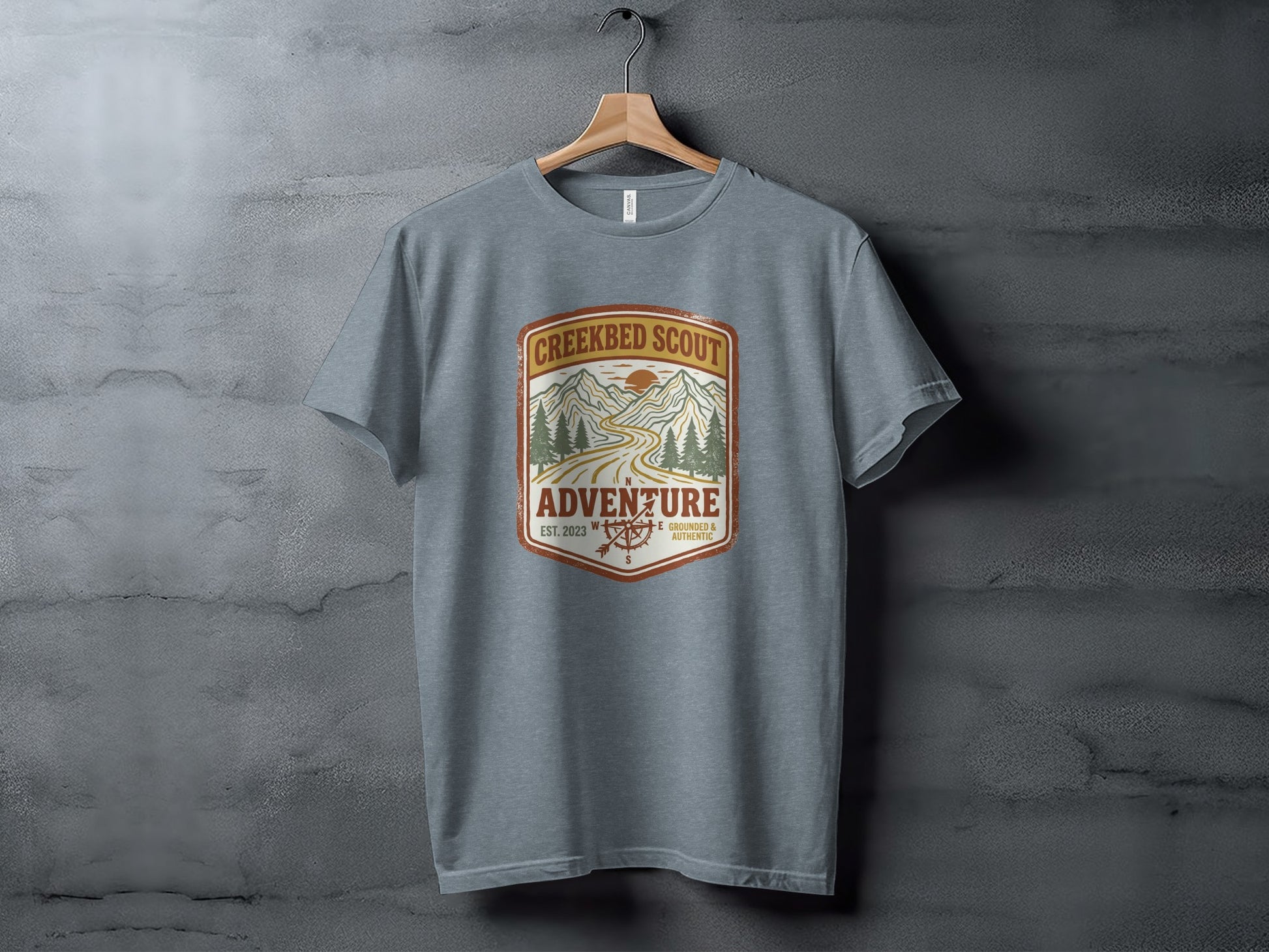 Rugged Creekbed Scout Adventure Emblem Wilderness Shirt: Grey t-shirt with Creekbed Scout Adventure logo featuring mountains, trees, and compass.