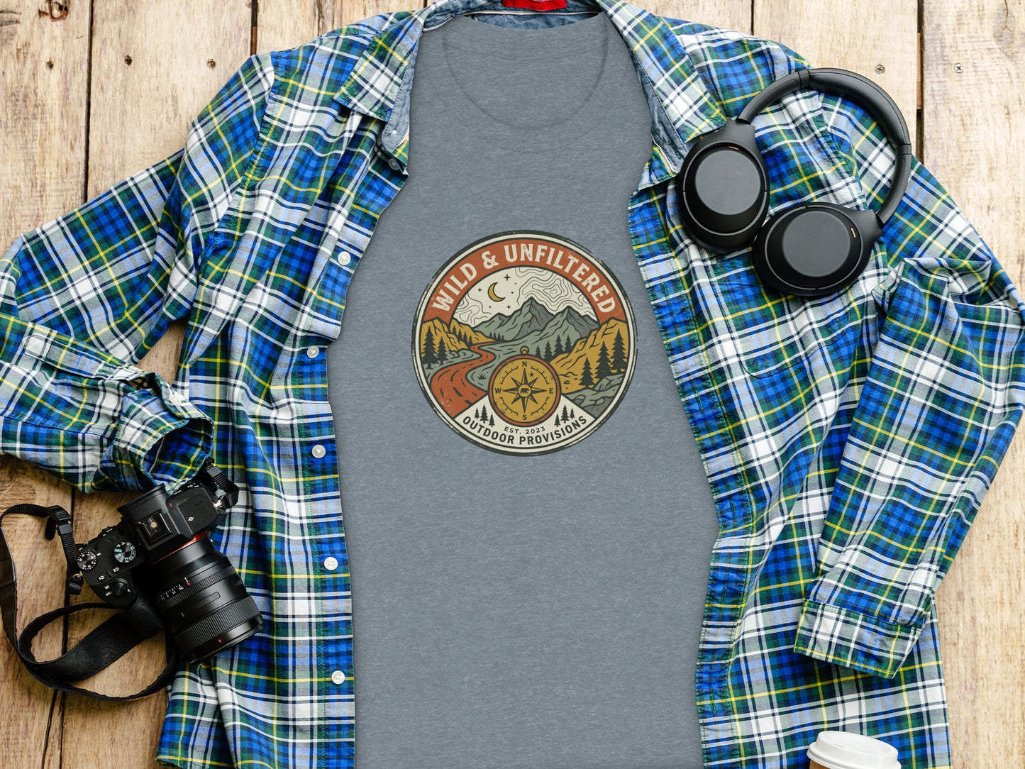 Rugged Wild & Unfiltered Explorer Wilderness Shirt: Flannel shirt, t-shirt with "Wild & Unfiltered Outdoor Provisions" logo, and headphones.