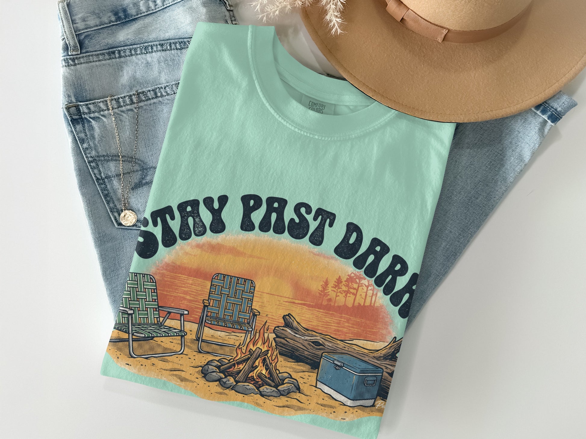 Mint green t-shirt with "STAY PAST DARK" text and sunset graphic, laid on jeans.