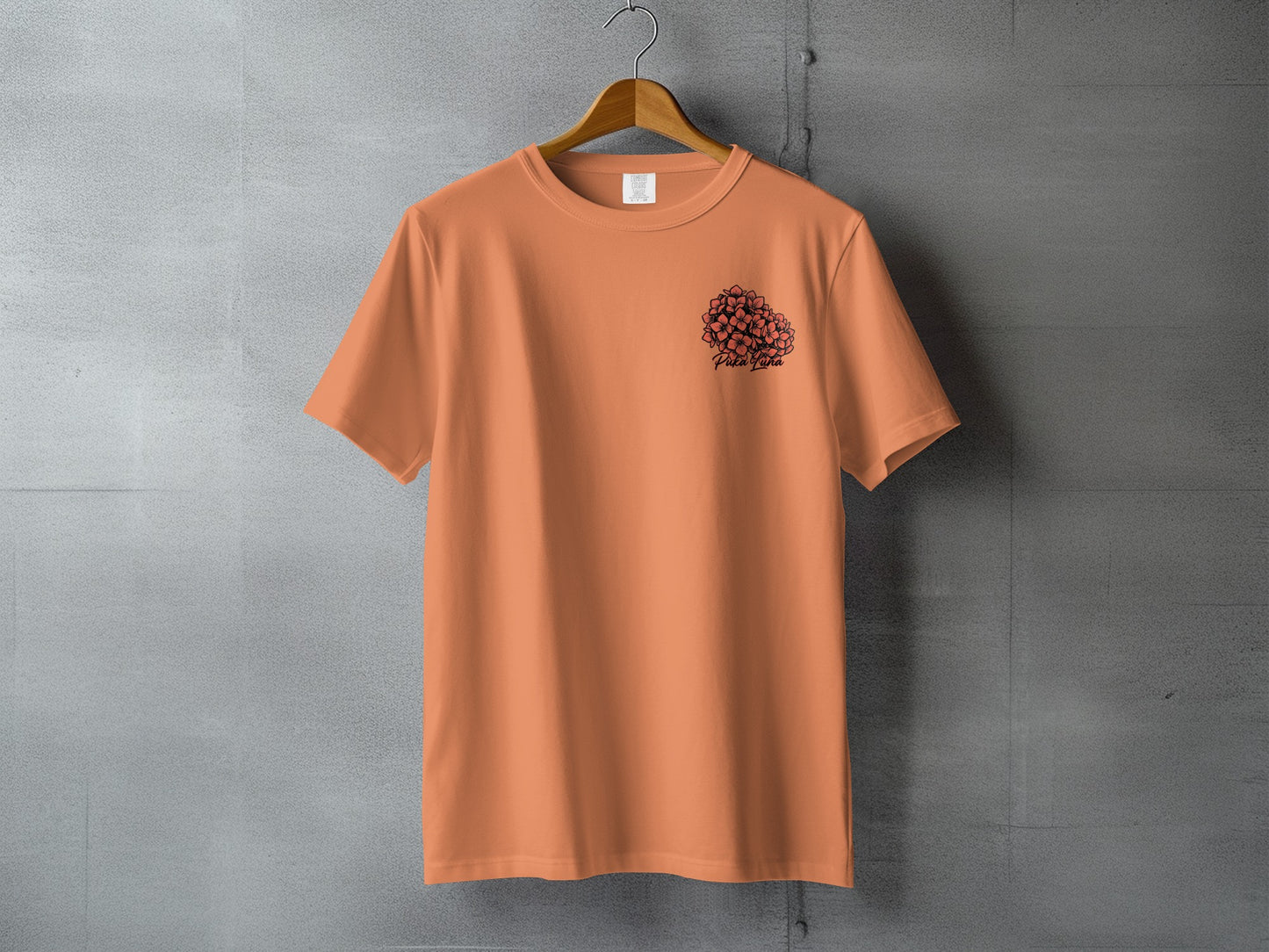 Orange t-shirt with black floral design and text "Pita Paha" on gray background.