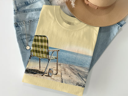 Yellow t-shirt with beach chair and ocean graphic, light brown hat, and jeans.