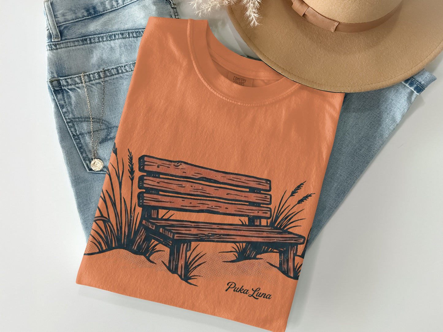 Orange t-shirt with a sketch of a park bench and grass.