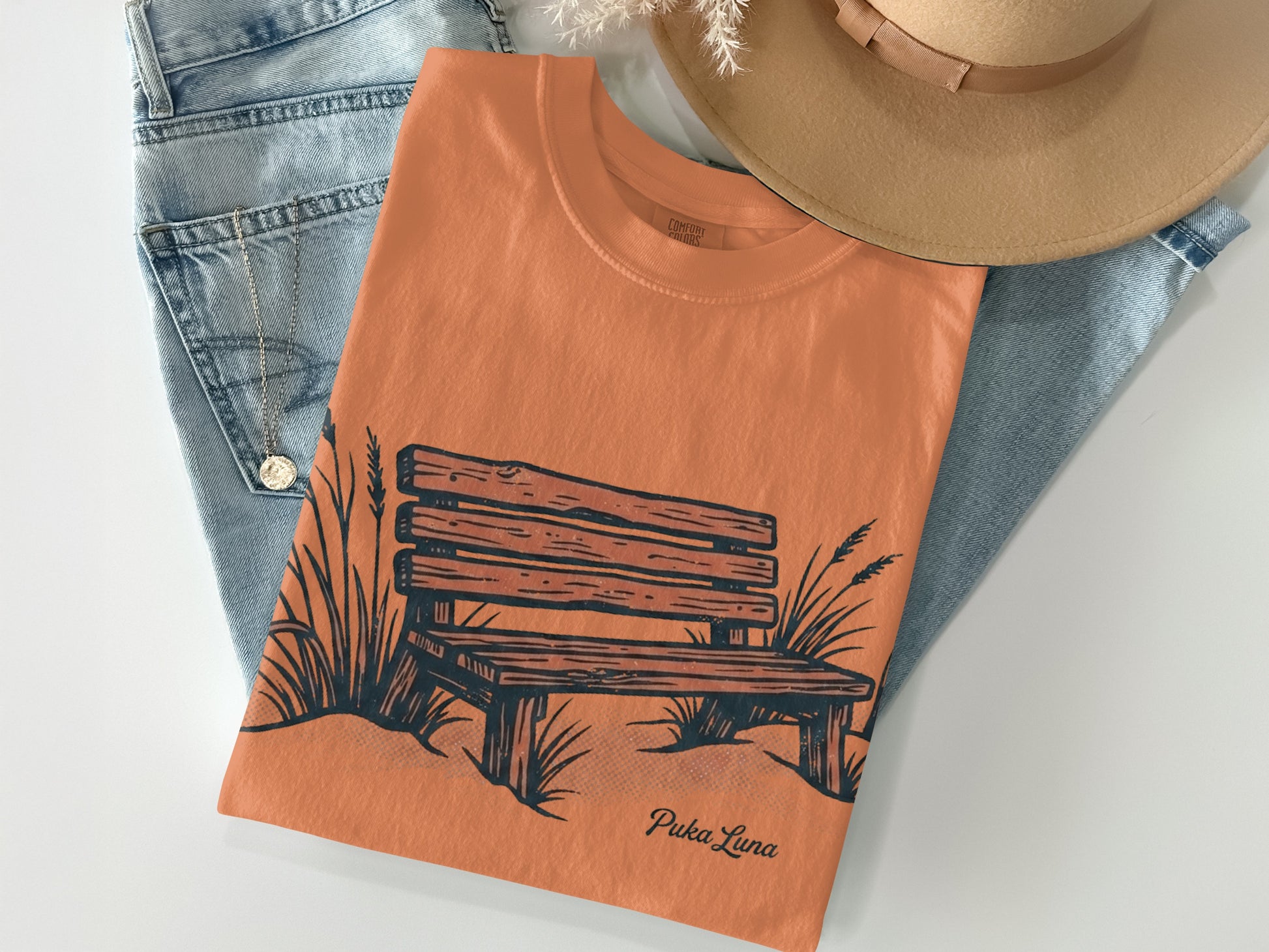 Orange t-shirt with a sketch of a park bench and grass.