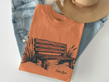 Orange t-shirt with a sketch of a park bench and grass.