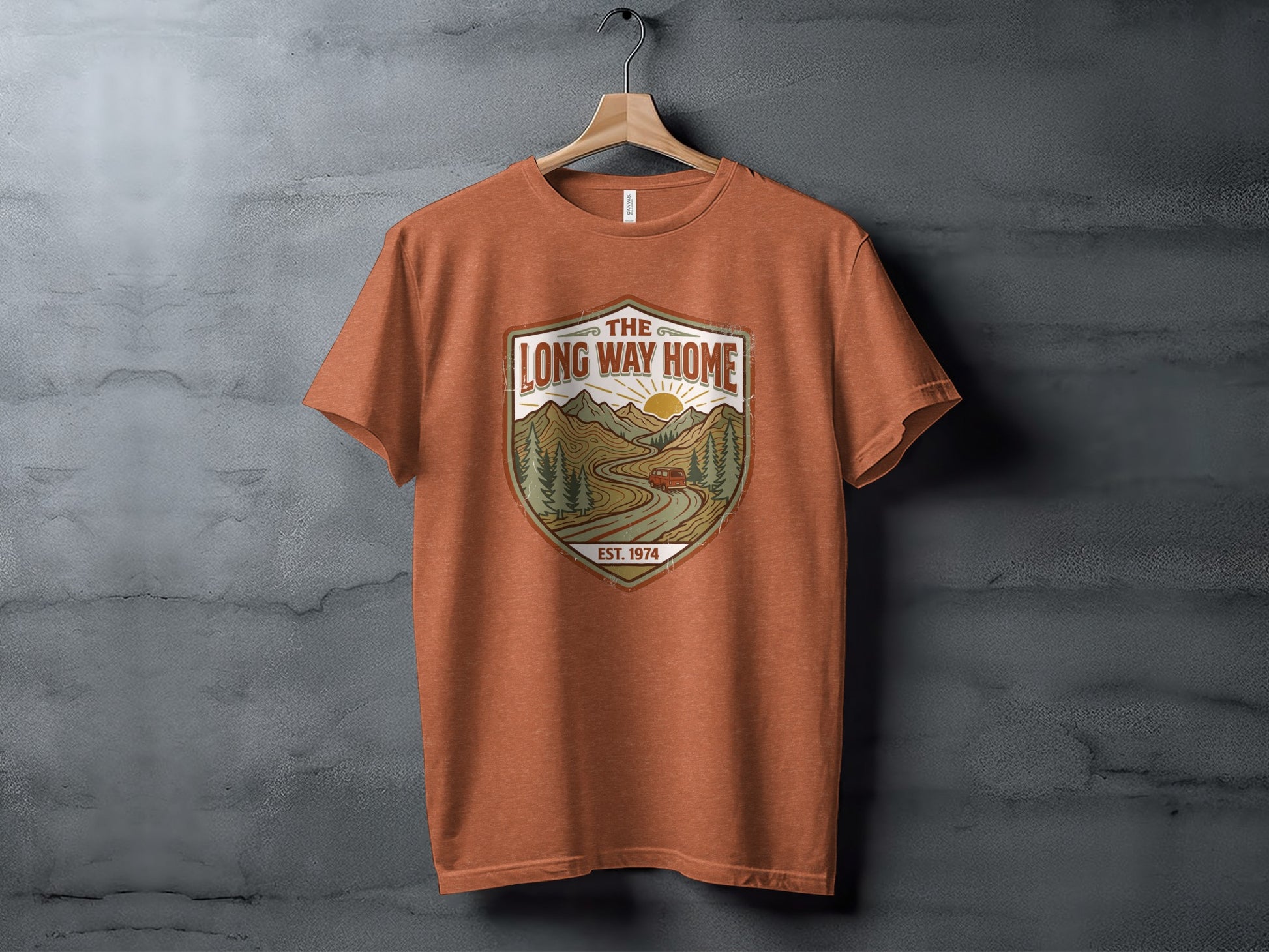 Rugged The Long Way Home | Vintage Adventure Wilderness Shirt: Orange t-shirt with a shield graphic of a road, mountains, and sun.