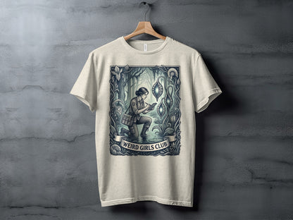 Cream t-shirt with "Weird Girls Club" text and an illustration of a woman exploring a fantasy landscape.