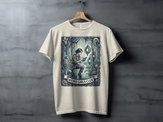 Cream t-shirt with "Weird Girls Club" text and an illustration of a woman exploring a fantasy landscape.