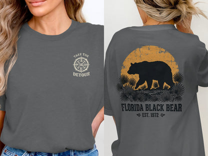 Front: Compass graphic with text "TAKE THE 16 DETOUR." Back: Black bear silhouette at sunset over grass.