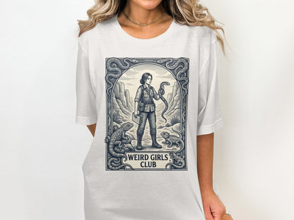 T-shirt graphic with woman holding snake, surrounded by lizards and desert landscape, text "WEIRD GIRLS CLUB".