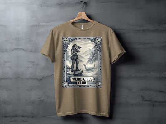 T-shirt with "Weird Girls Club" text and a woman observing a dinosaur in a scenic landscape.