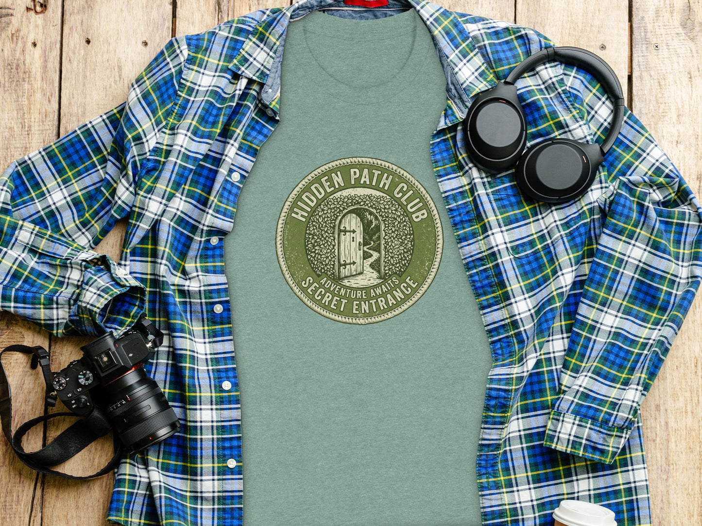 Hidden Path Club: Secret Entrance | Vintage Outdoor Apparel: Green t-shirt with "Hidden Path Secret Entrance" circular logo, laid flat with camera and headphones.