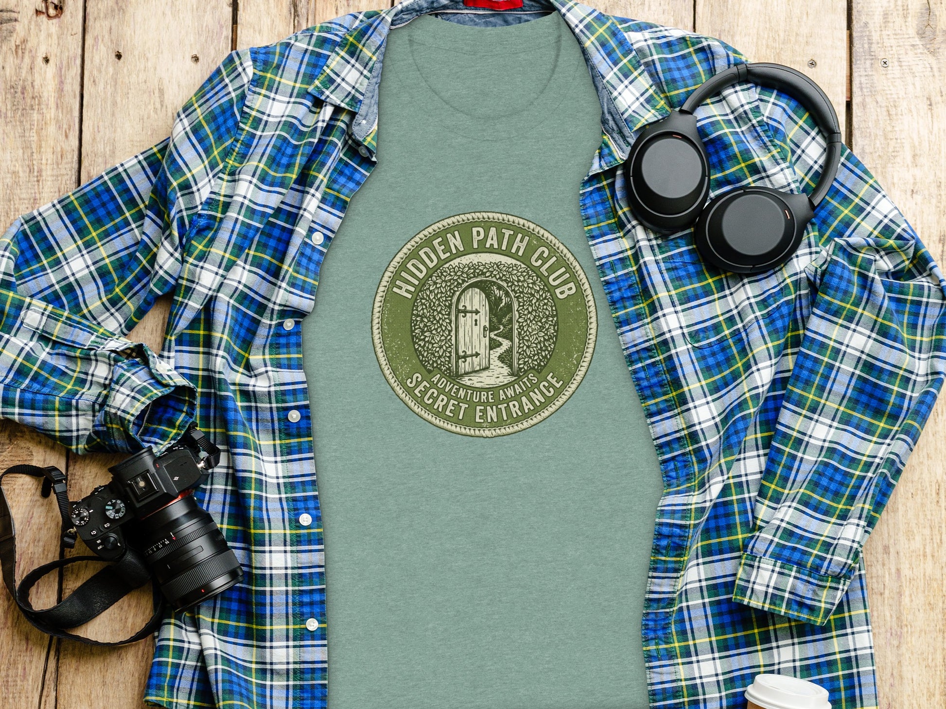 Hidden Path Club: Secret Entrance | Vintage Outdoor Apparel: Green t-shirt with "Hidden Path Secret Entrance" circular logo, laid flat with camera and headphones.