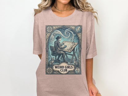 T-shirt featuring a woman at a drafting table with cats and celestial designs.