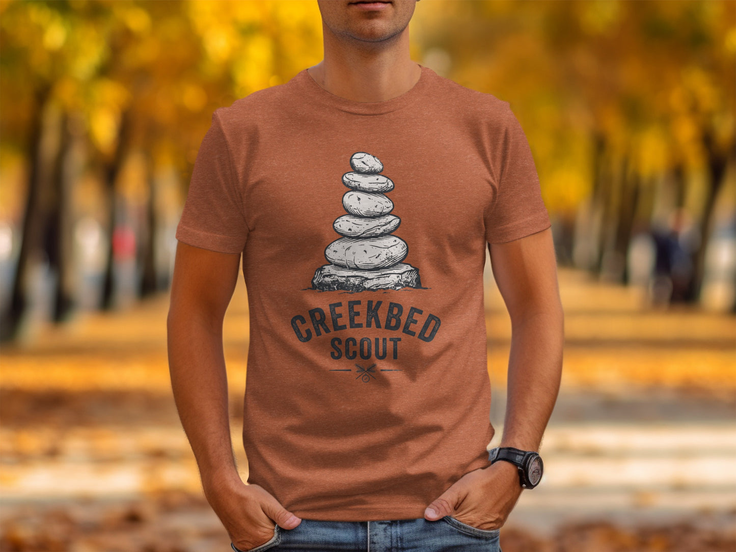 Creekbed Scout Cairn Graphic: The Explorer's Adventure Tee: T-shirt with stacked stones and "Creekbed Scout" text on a blurred autumn background.