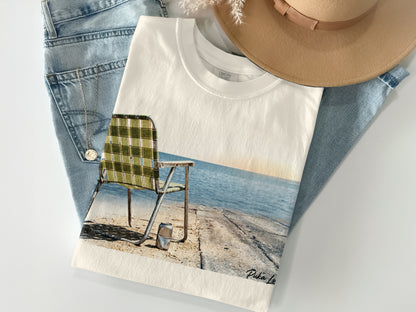 White t-shirt with graphic of a weathered beach chair overlooking the ocean.