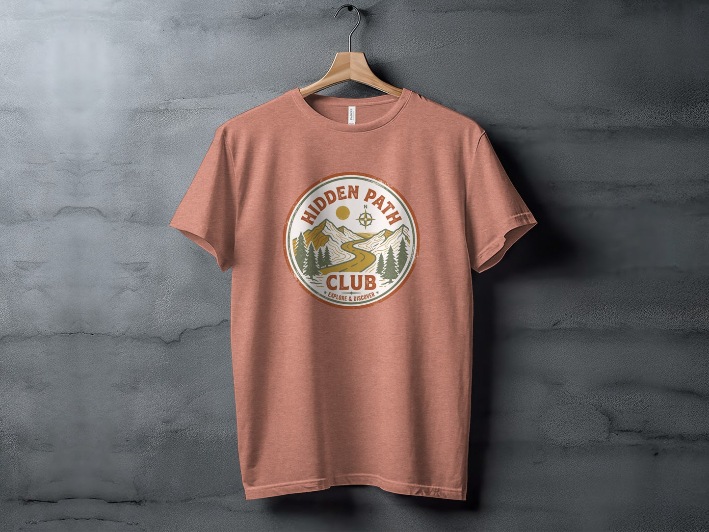 Rugged Hidden Path Club Explorer Wilderness Shirt: Salmon t-shirt with "Hidden Path Club" circular logo featuring mountains, trees, and a winding path.